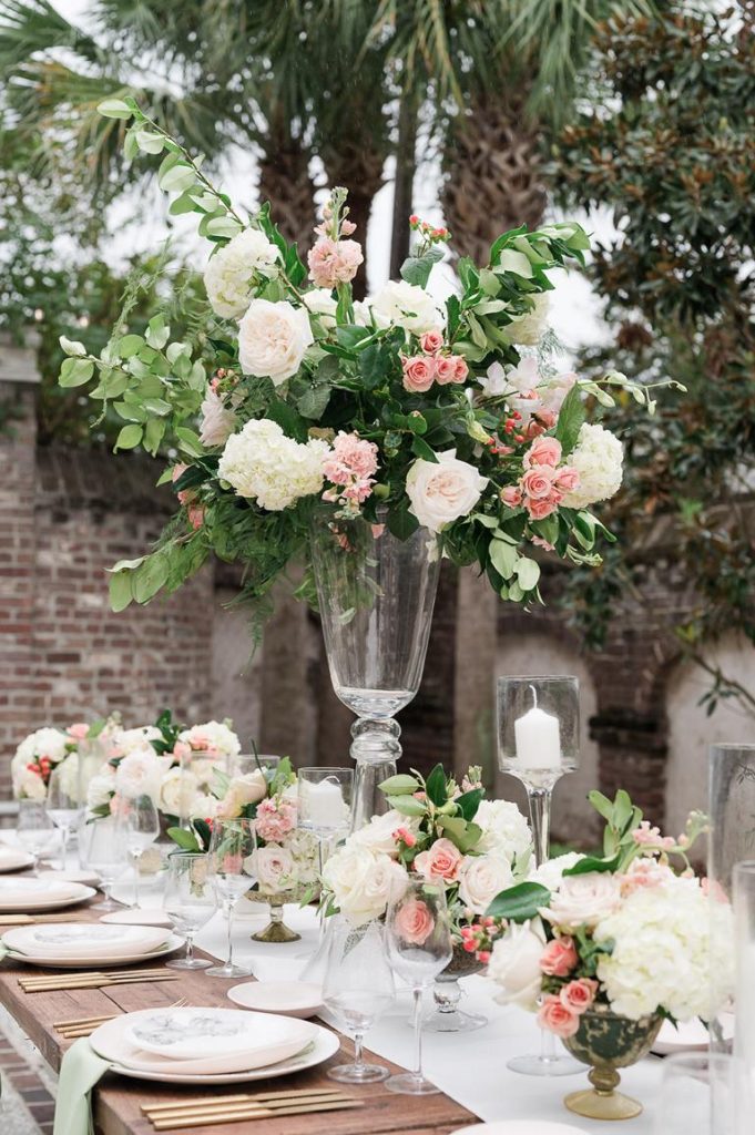 table at wedding reception with mulitple vases of flowers and tall vase of flowers