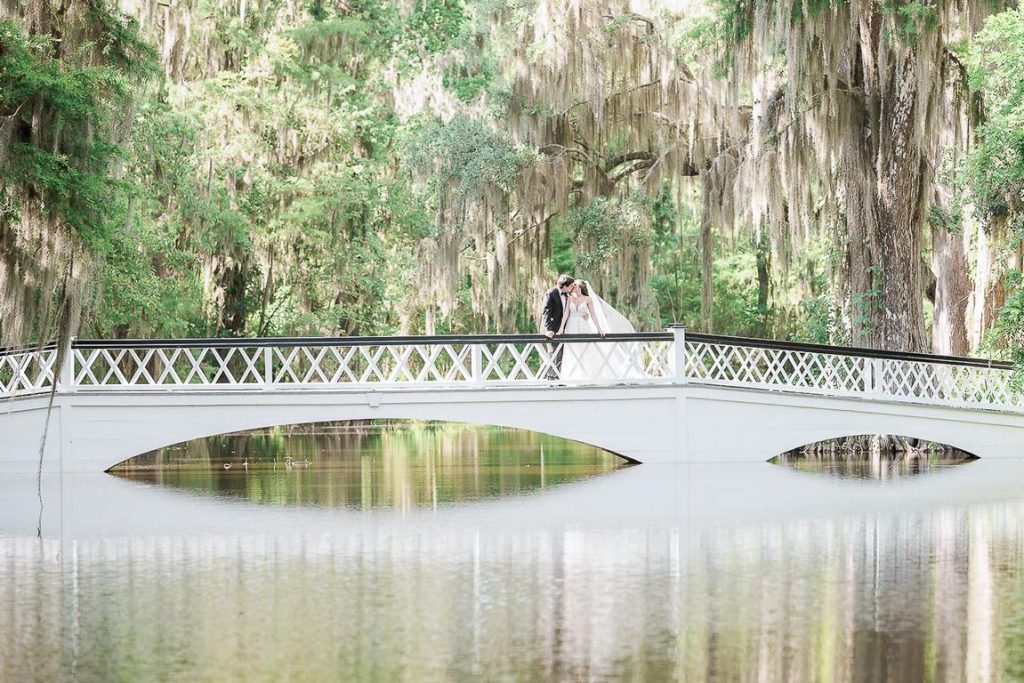 newlyweds kiss on white bridge in Magnolia plantation