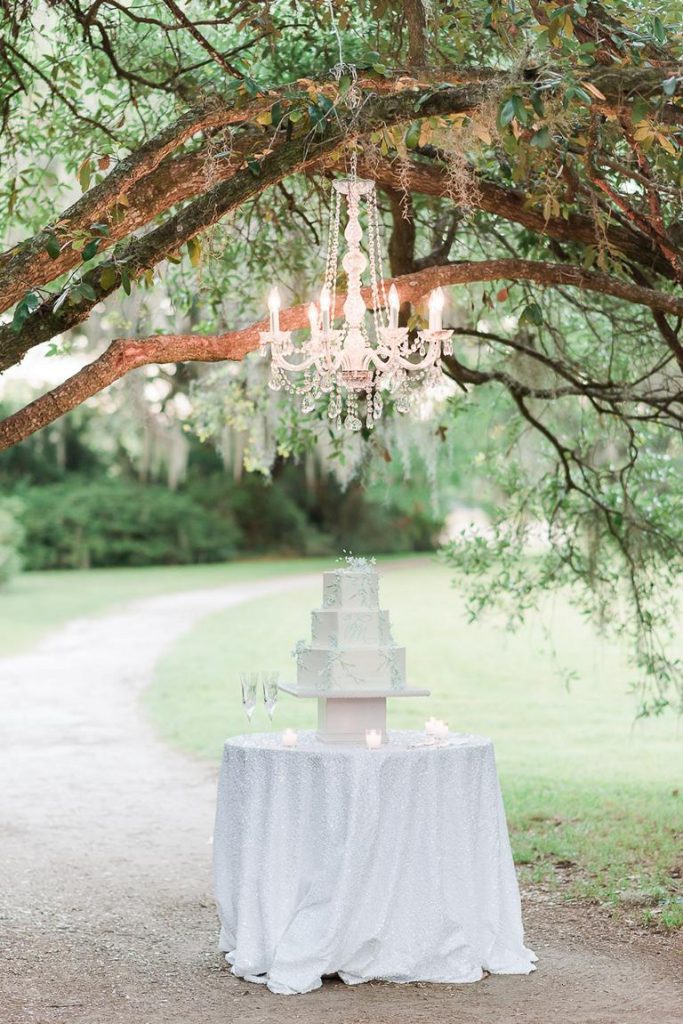 3 tiered white wedding cake outside under lit chandelier