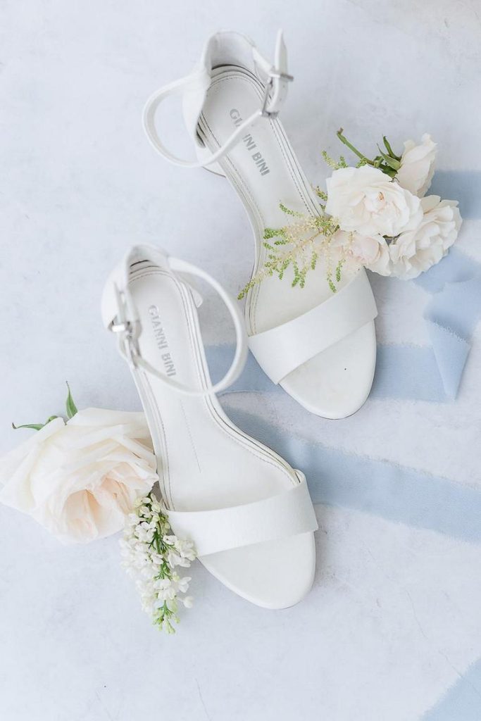 flat lay with white wedding heels and blue ribbon and white flowers