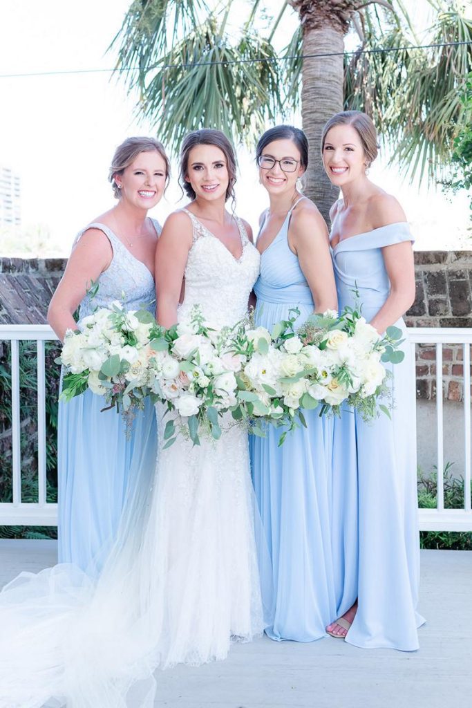 bride and bridesmaids in pale blue dresses standing close with white bouquets touching