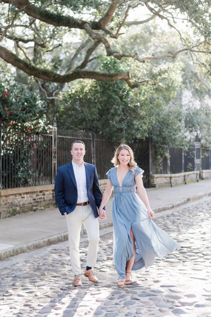 couple walking hand in hand on cobblestone street with iron fence in background, Engagement and Wedding Photography Galleries