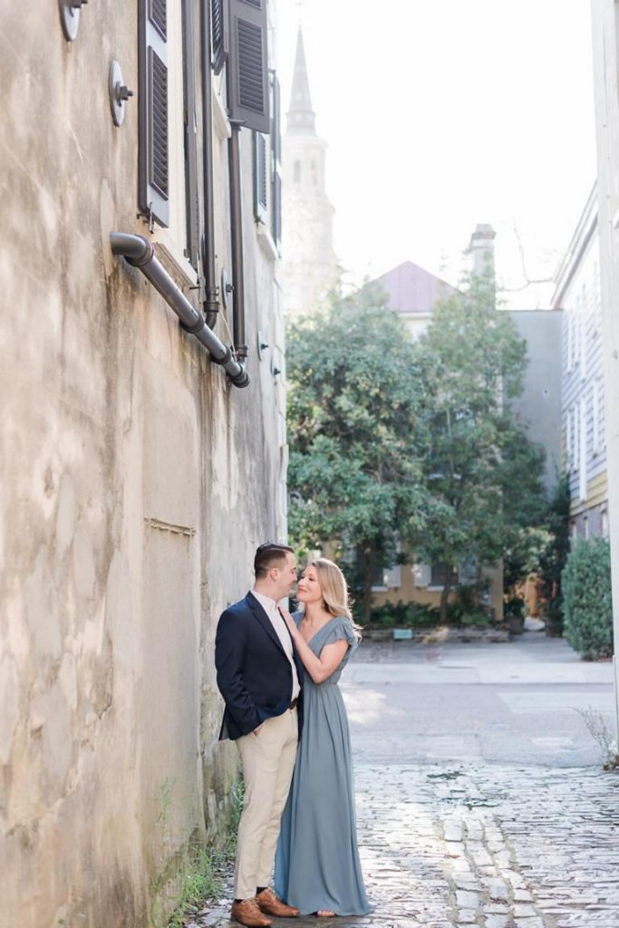 Couple in cobblestone alley with church steeple in background