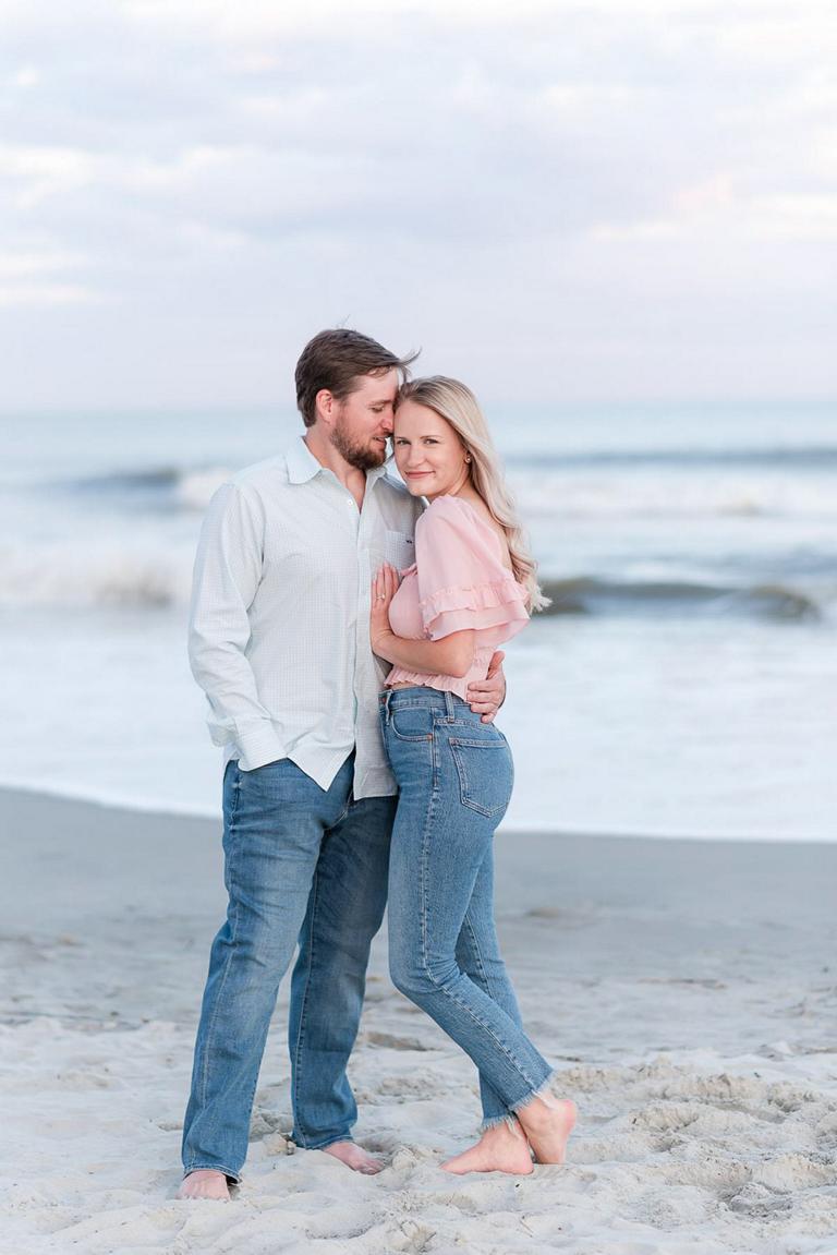 guy nuzzling into girlfriend's hair while standing at beach