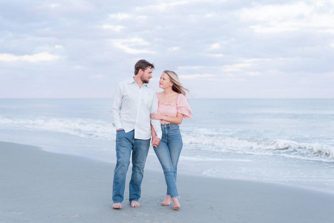 couple holding hands walking at beach while looking into each other's eyes