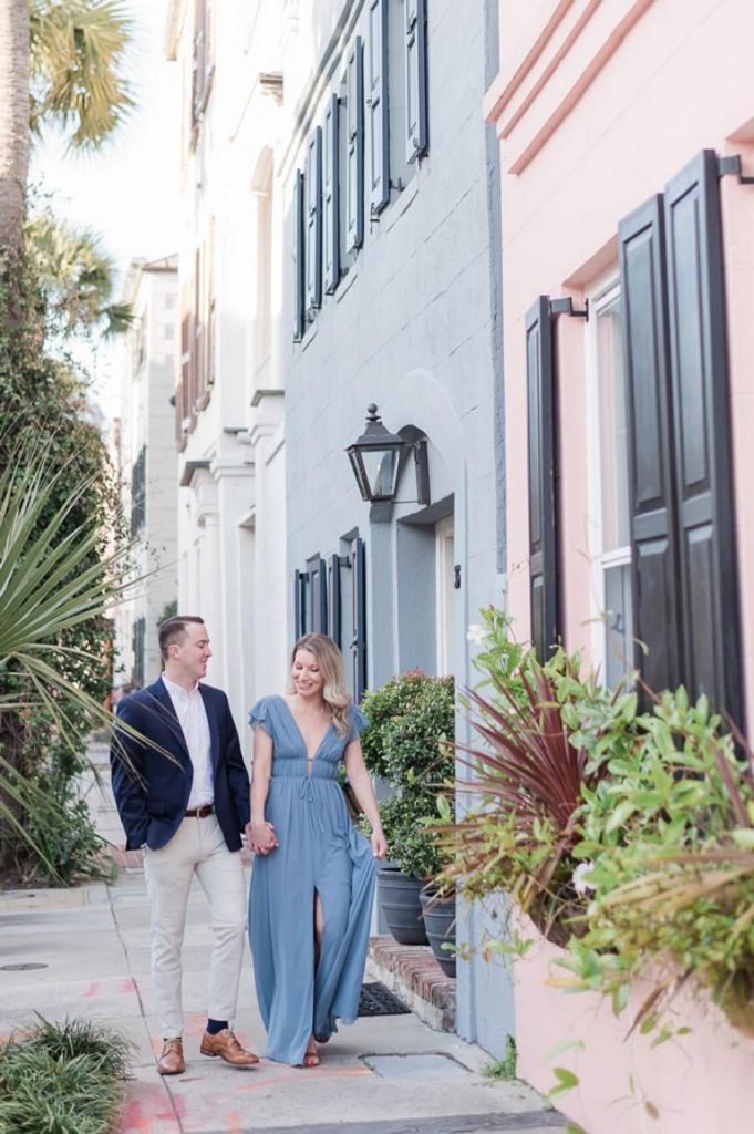 engaged couple walk hand in hand down historic street in Charleston with rainbow colored houses
