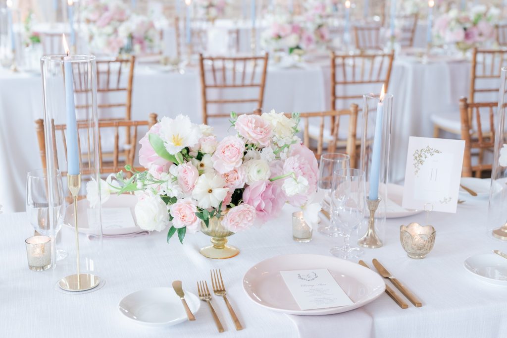 table setting with white and blush flowers, gold silverware, pink plate, light blue candles