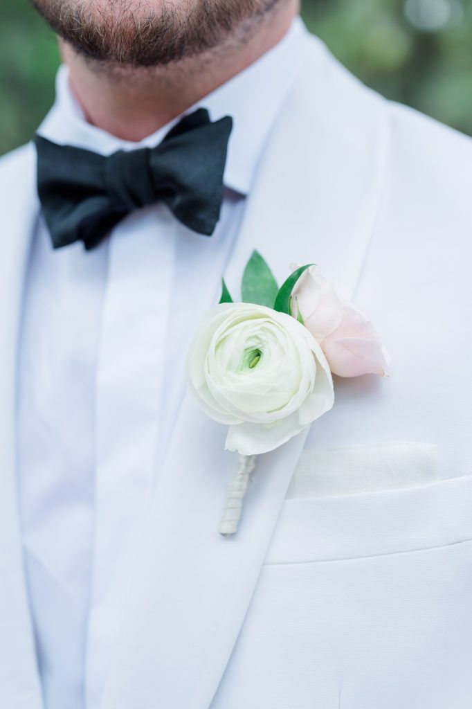 close up of groom's white tuxedo , black bowtie, and white and blush floral boutineer