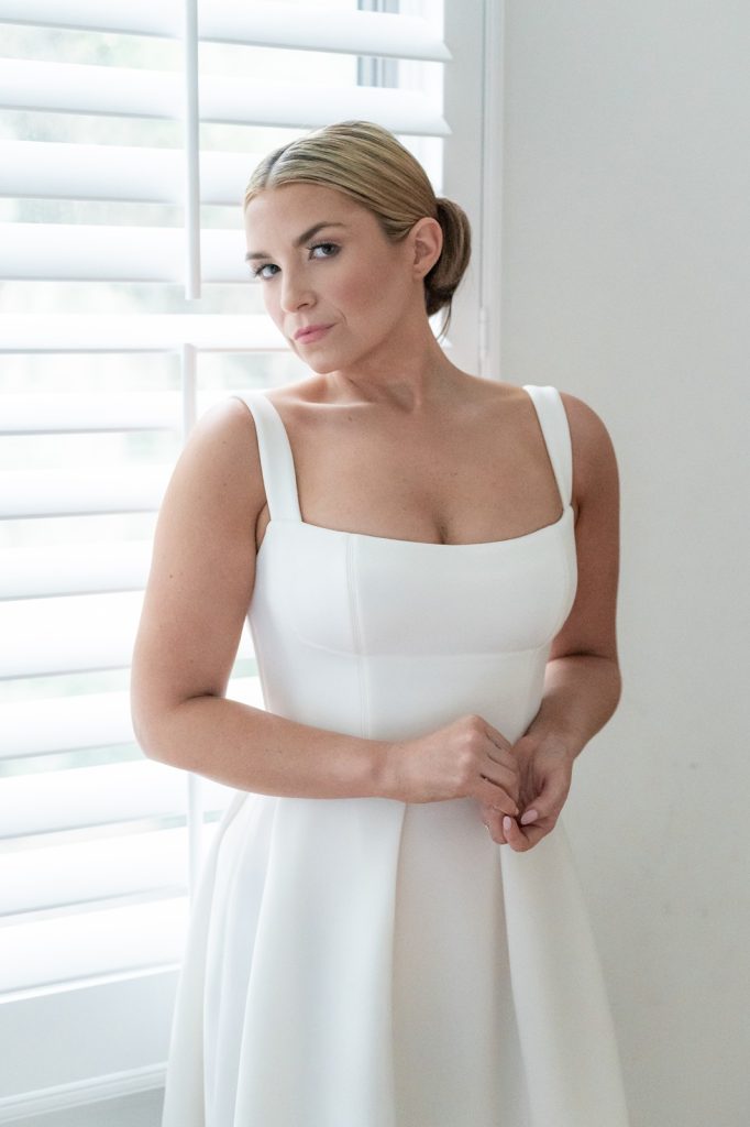 bride holding hands and looking at camera in front of white shutters