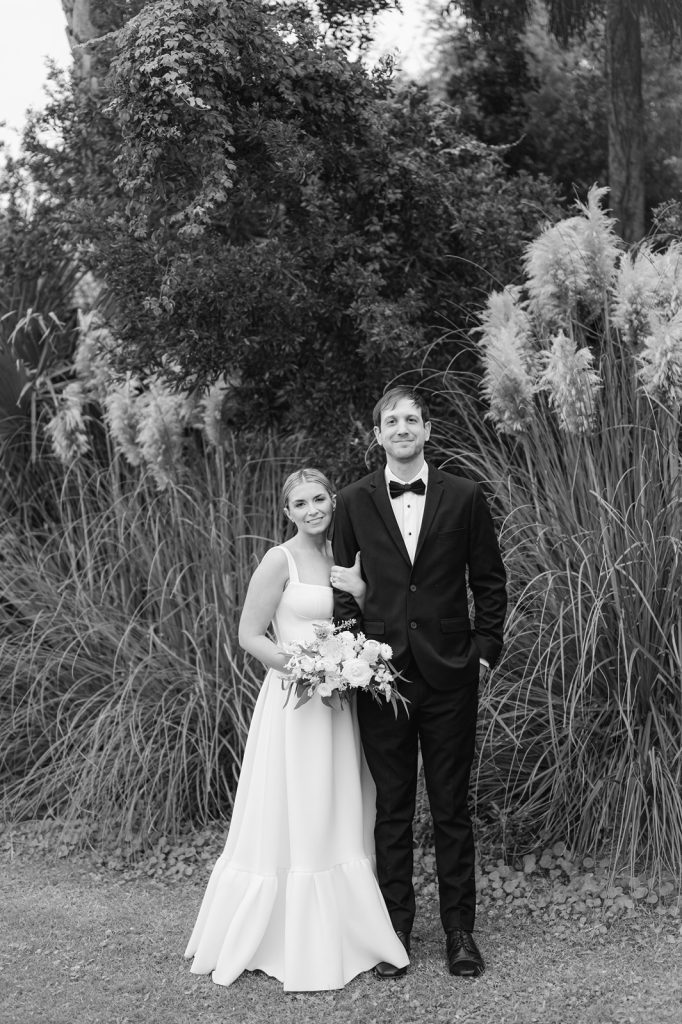 bride snuggles onto groom's arm in front of pampas grass