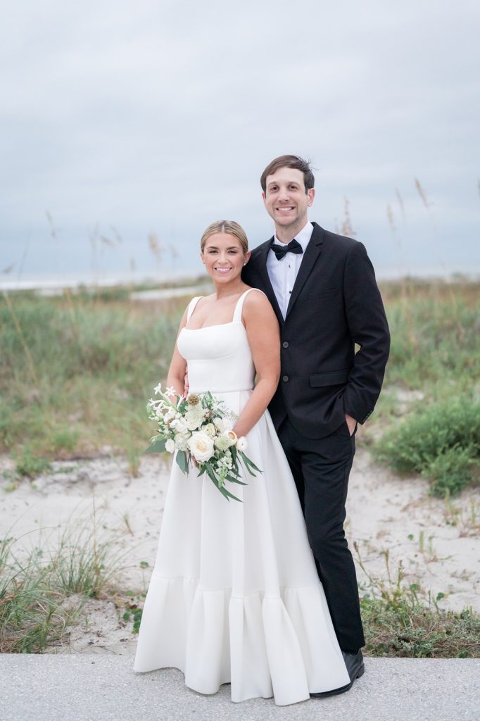 bride and groom look at camera with beach in the background
