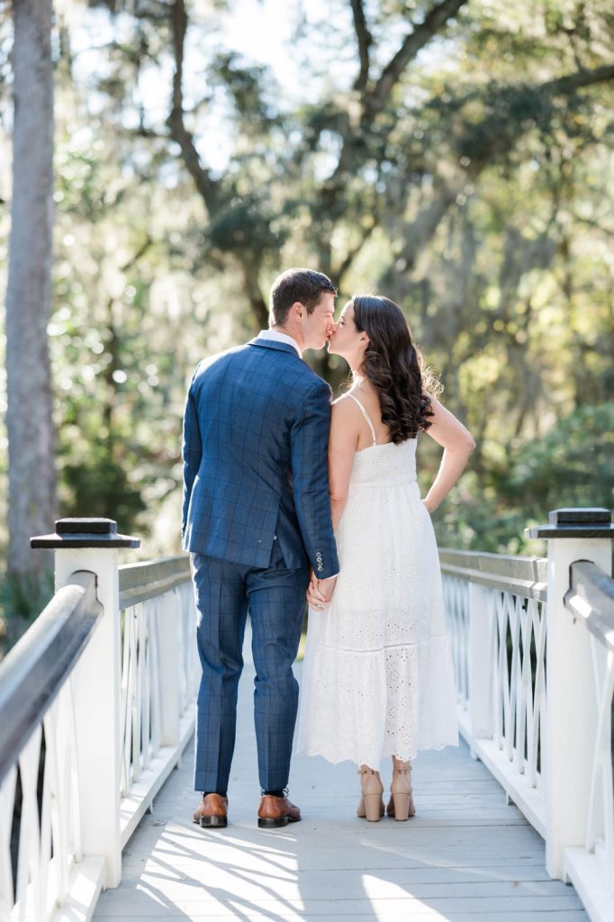 engaged couple kiss with backs towards camera on white bridge