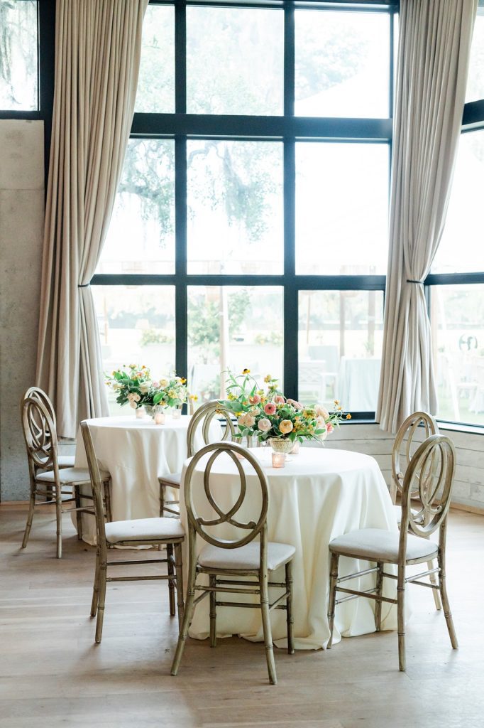 interior photo of wedding reception with tables with wooden chairs and floral arrangements on top