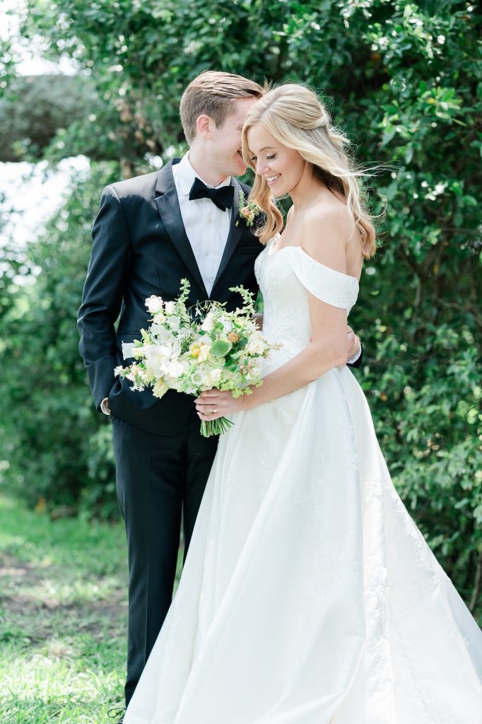 groom whispers in bride's ear as she smiles