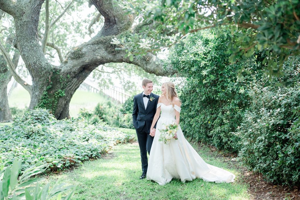 newlyweds walk holding hands looking at each other in garden