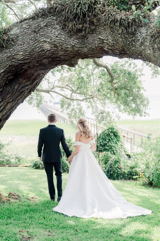 newlyweds hold hands and walk away towards water
