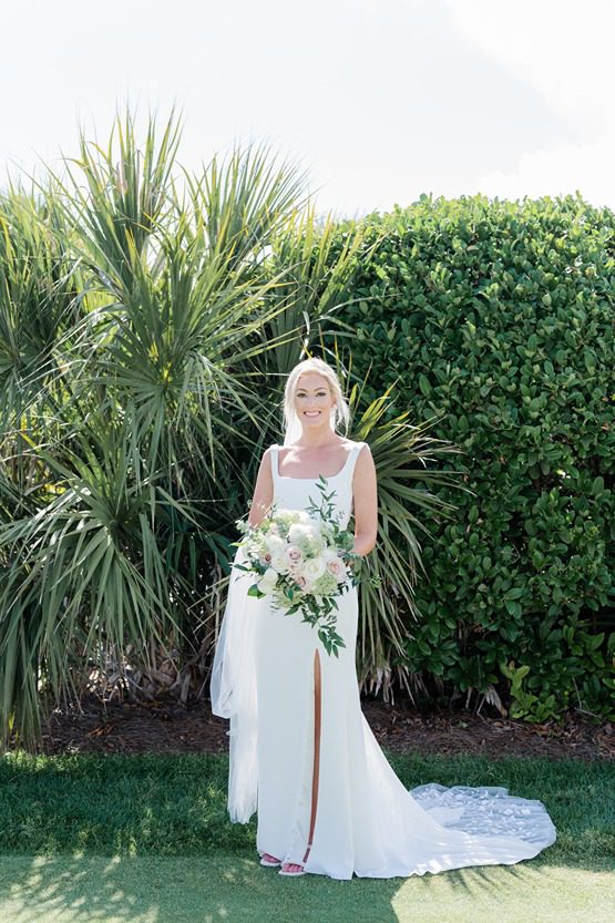 full length bridal portrait of bride looking directly at camera in front of greenery
