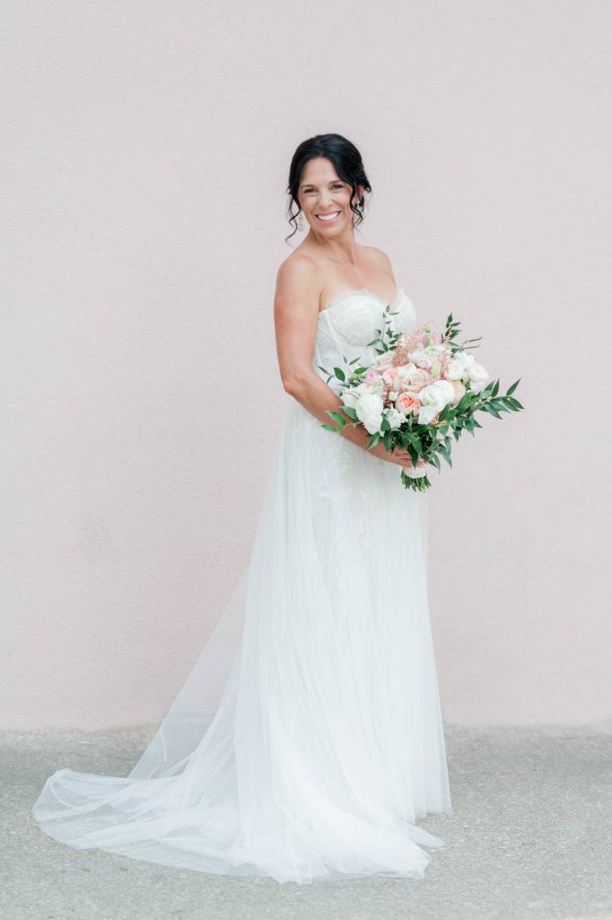 brunette bride standing in front of pink wall in tulle wedding dress