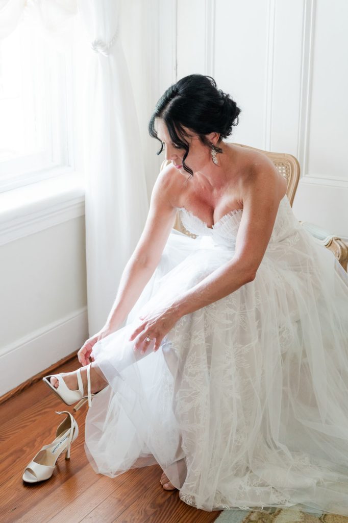 bride sitting down putting her shoes on near window