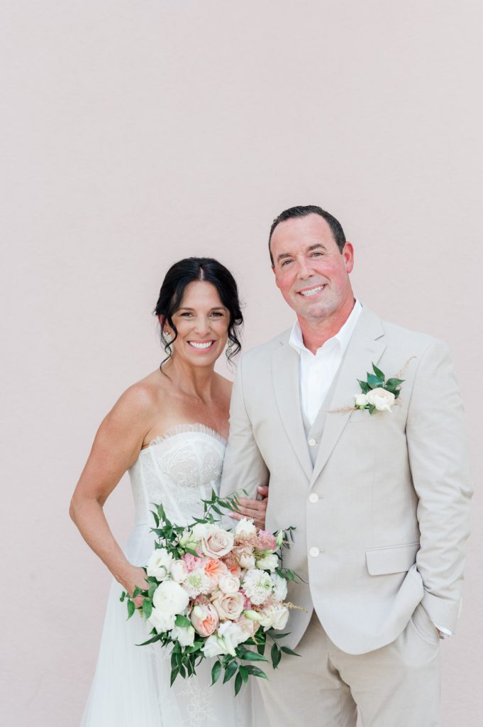 bride holds on to groom's arm in front hotel exterior pink wall
