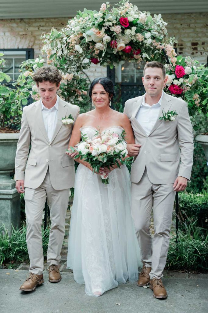 Bride processing down aisle with sons at either side under floral arch at the Parsonage