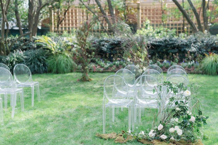 Outdoor wedding ceremony set up with clear chairs and arch made of branches and roses