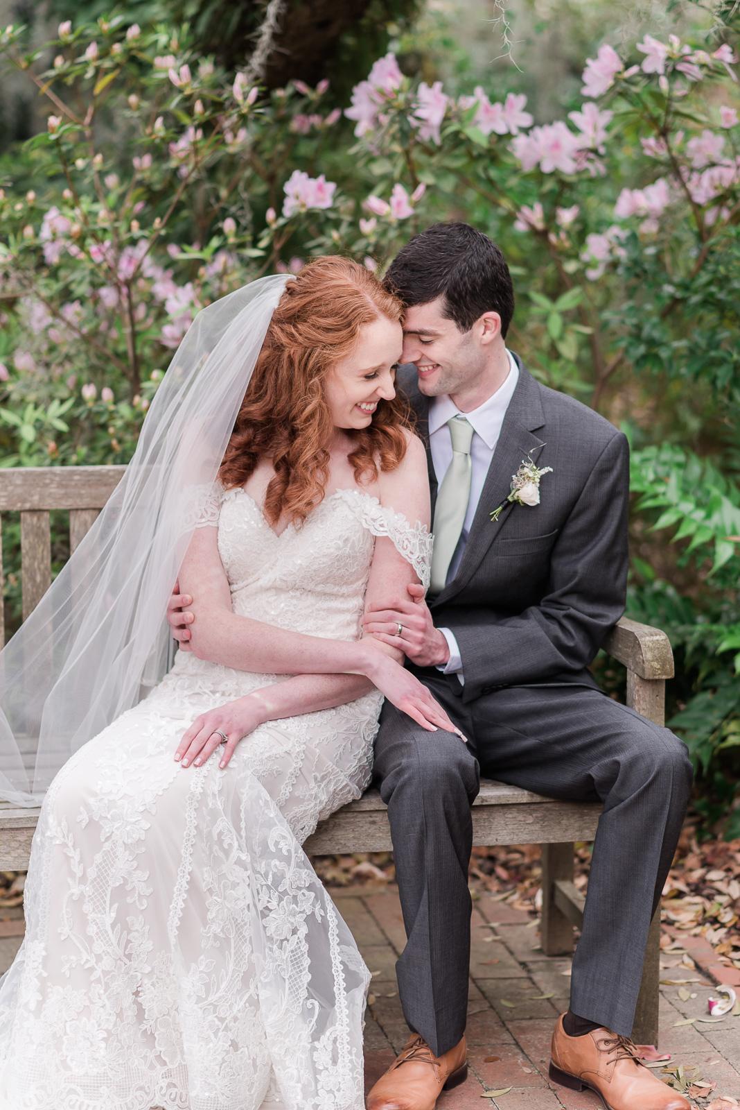 Newlywed couple snuggle on park bench surrounded by pink flowers