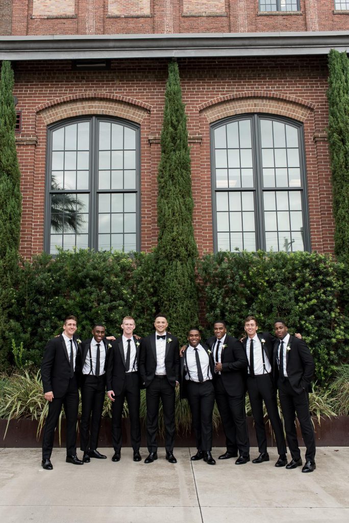 groom and groomsmen stand with arms around each other in courtyard