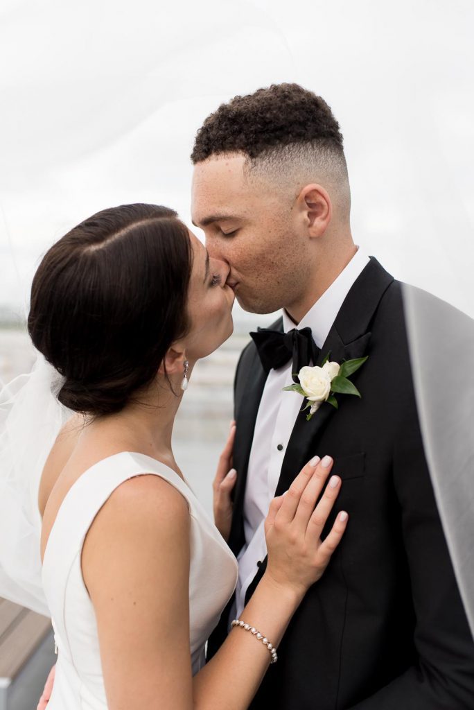 newlyweds kiss under bride's veil on rooftop of Cedar Room