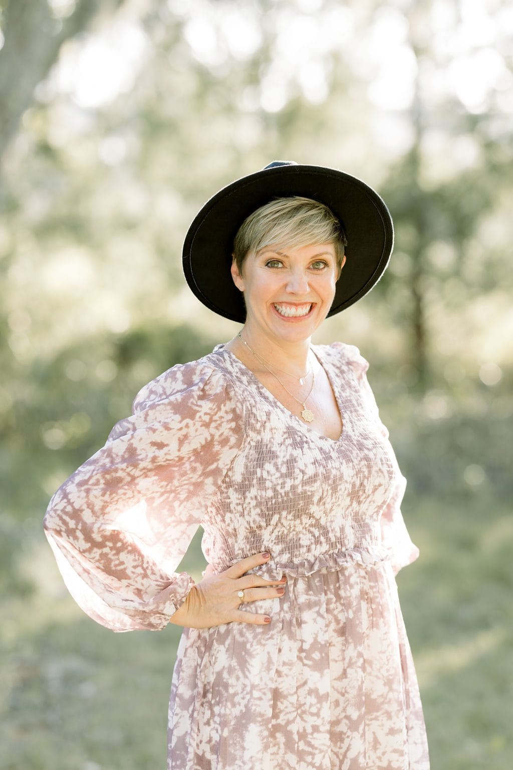Photographer Leigh Hayward wearing a black hat and tie dyed dress stands with hand on hip