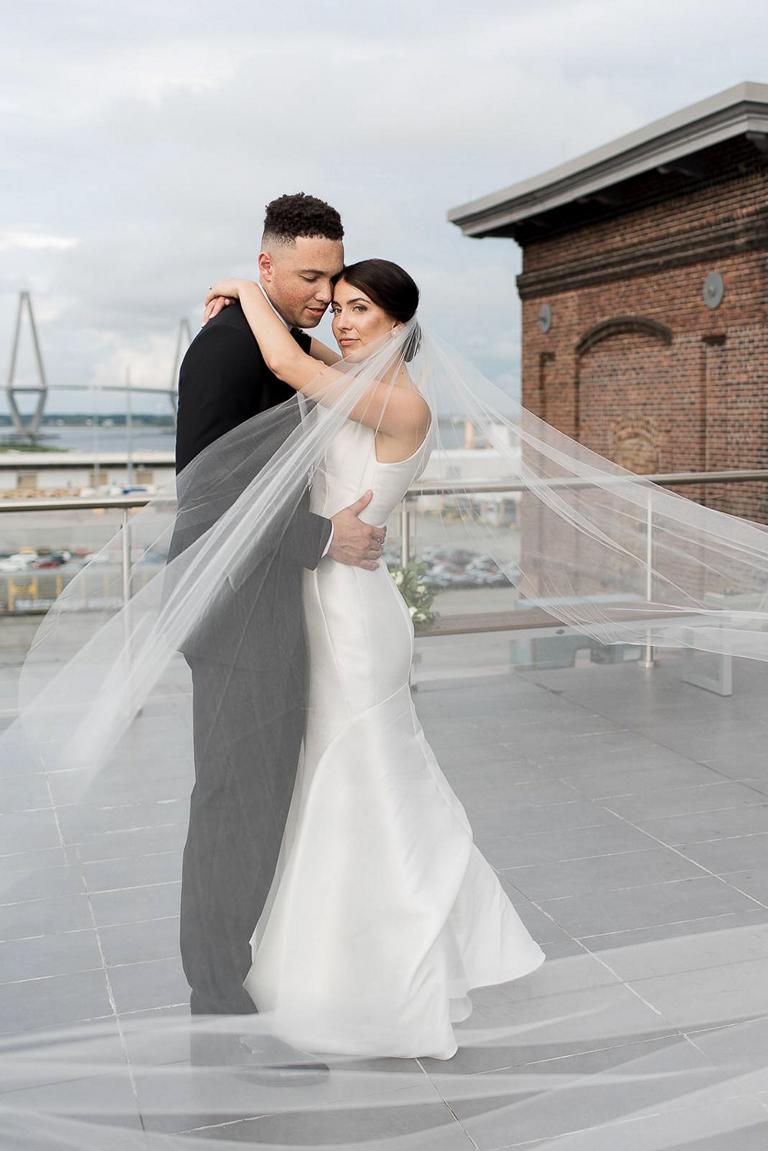 newlywed couple hug each other under bride's veil on top of the roof of the Cedar Room