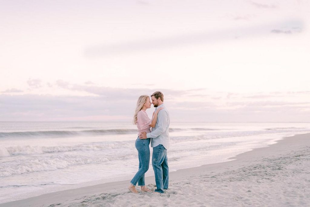 Couple stand nose to nose at pink sunset on beach