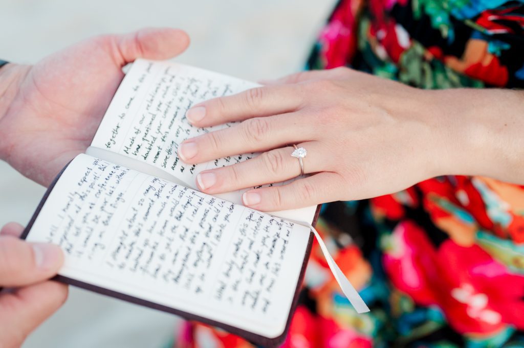 girl puts hand with new engagement ring on top of journal her fiancé used to propose to her