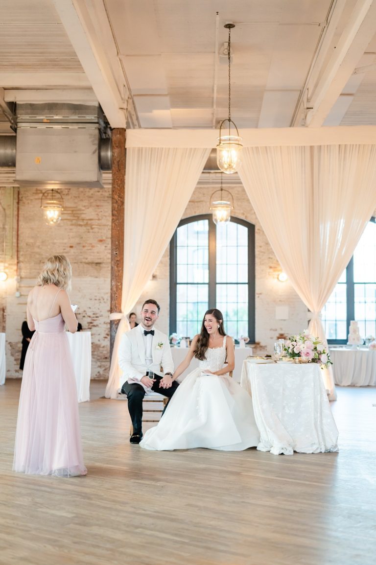Coupe looks on laughing as Maid of Honor gives toast at their wedding