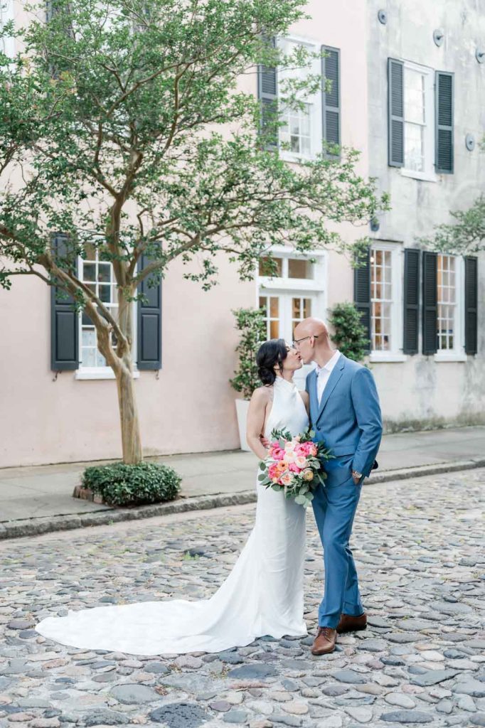 newlywed couple kiss while standing on cobblestone street