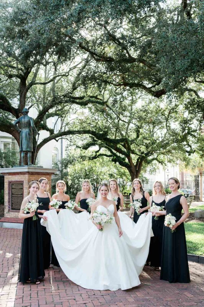 bridesmaids hold wedding dress of bride while walking in Washington square park
