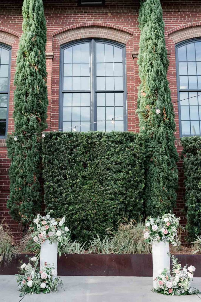 outside wedding ceremony set up with two white columns with floral arrangements on top and on the ground in front of them