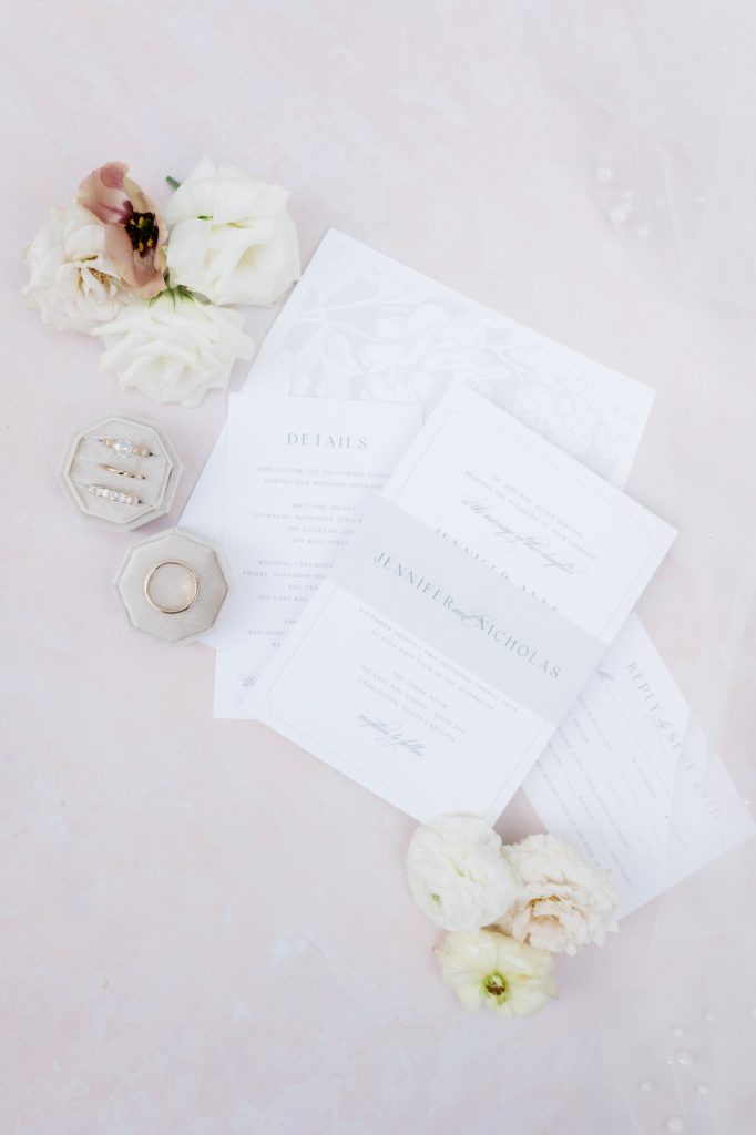 Wedding invite suite, rings, and flowers displayed on pink background