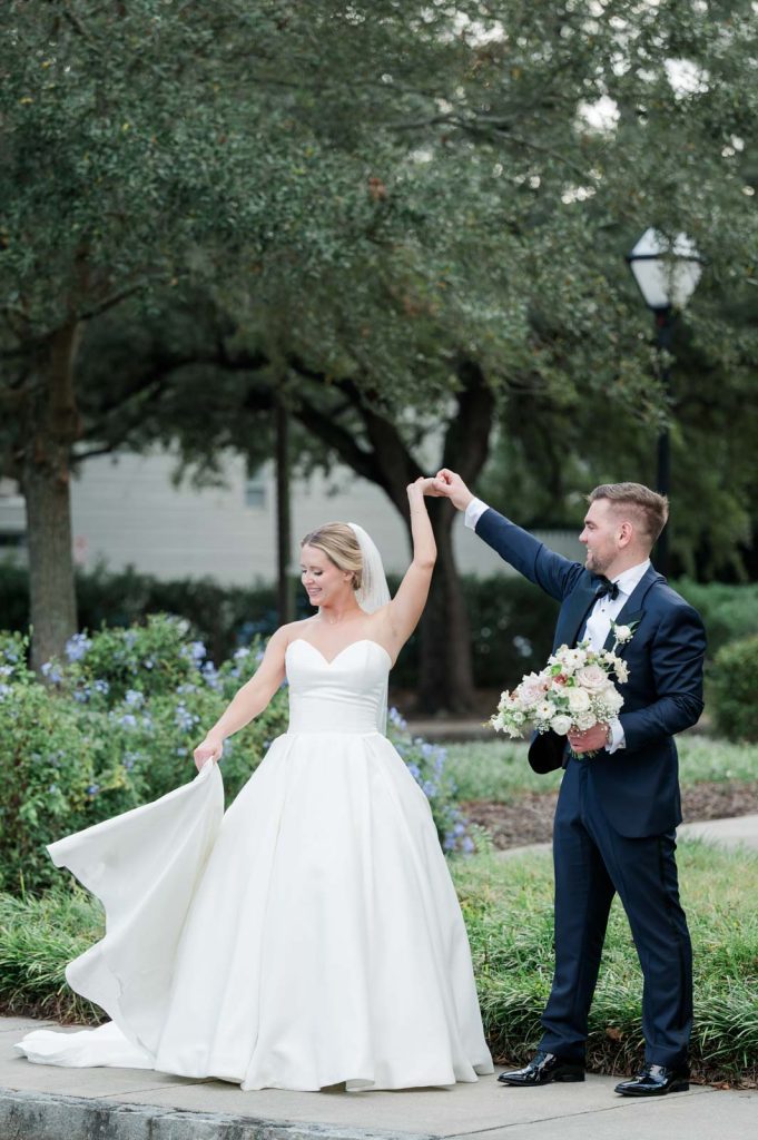 groom twirling bride in park while holding her bouquet