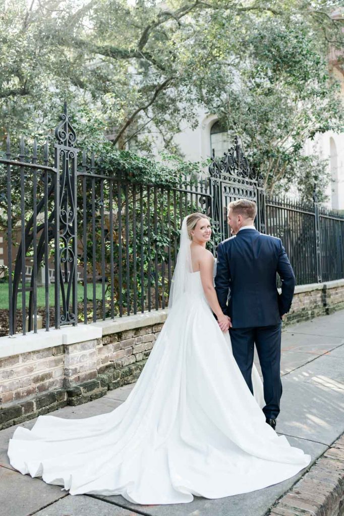 back of bride and groom holding hands in front of the black iron fence of Washing to square park in Charleston, SC