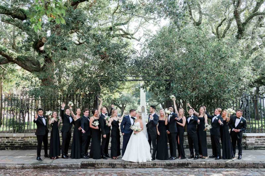 large wedding party dressed in black cheering whole bride and groom kiss on Chalmer's Street