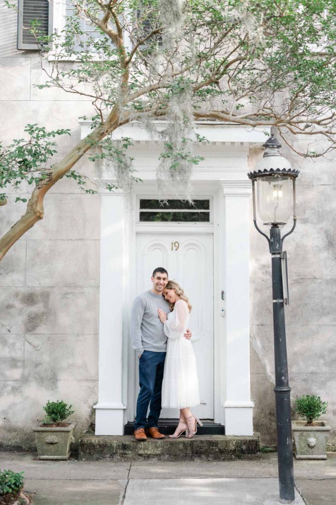 engaged couple stand in door frame, girl leans head on guy's shoulder