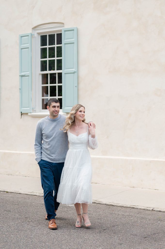 guy hugs girl around shoulder while walking away from yellow building