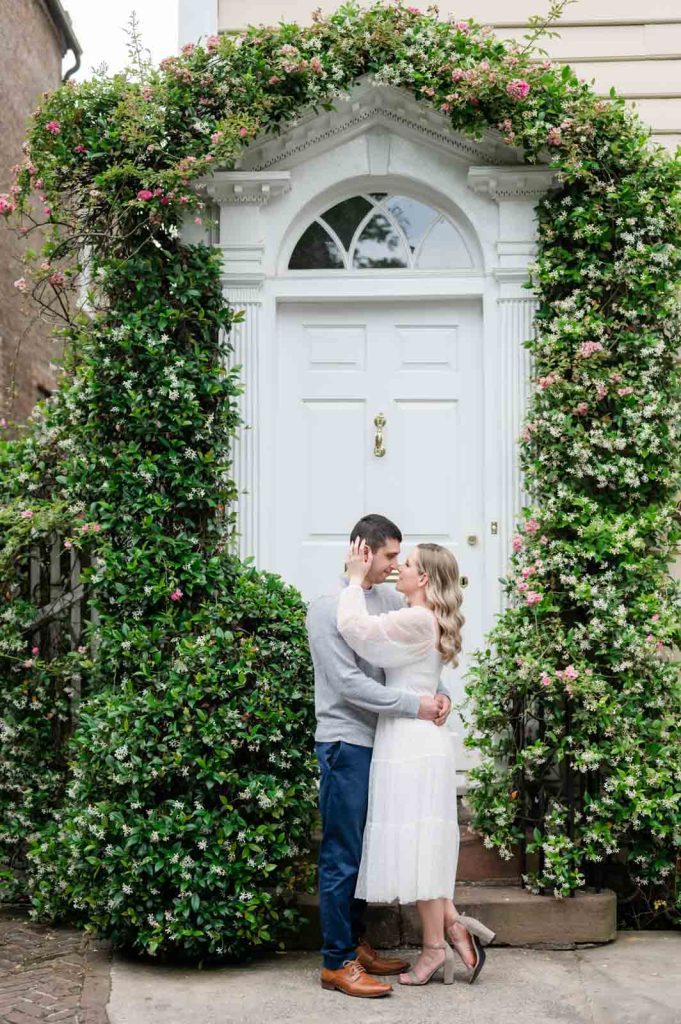 couple almost kisses in front of door with jasmine growing around it