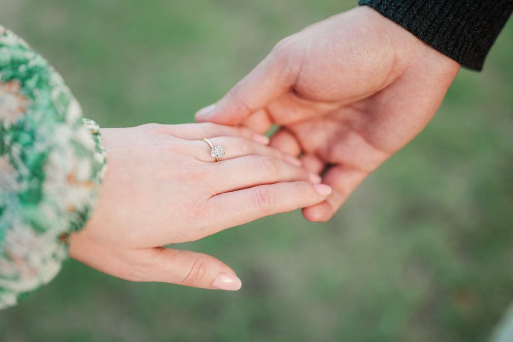 close up of two hands touching one with an engagement ring