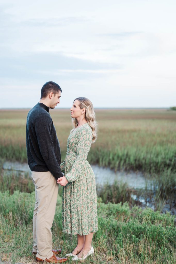 engaged couple hold hand down low with marsh in the background